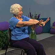 a woman sitting in a chair stretches her arms and fingers forward while laughing